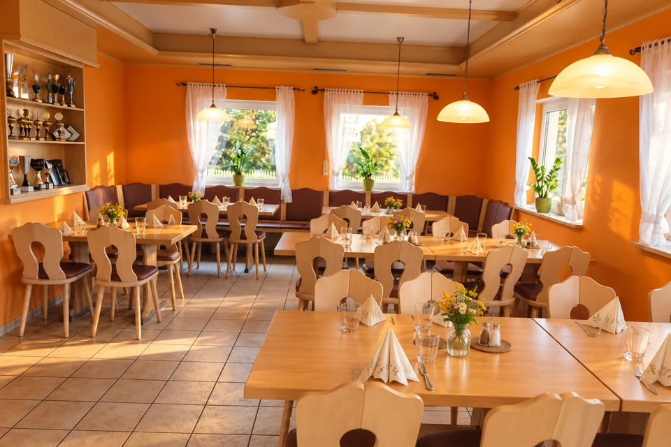 Warmer Gastraum mit hellen Holztischen und orangefarbenen Wänden